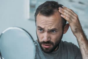 man in front of a mirror noticing that he have more hairloss than usual