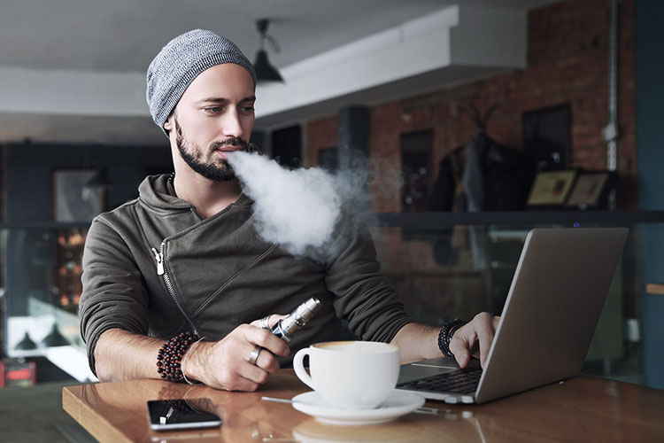 man vaping cbd and having a coffee while browsing the internet